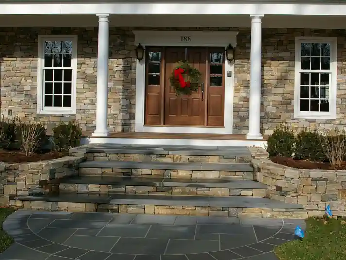 Custom designed front steps with bluestone treads, bluestone tiles and New England fieldstone retaining wall.